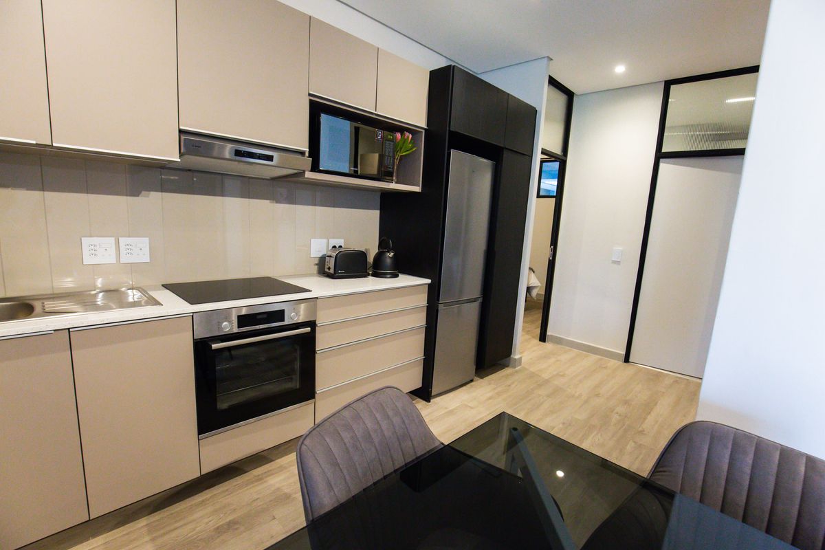 Modern kitchen featuring sleek beige cabinetry, integrated appliances including an oven and hob, and durable laminate flooring in a contemporary apartment setting.