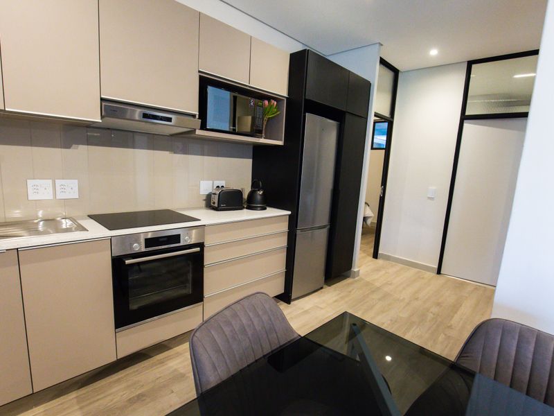 Modern kitchen featuring sleek beige cabinetry, integrated appliances including an oven and hob, and durable laminate flooring in a contemporary apartment setting.