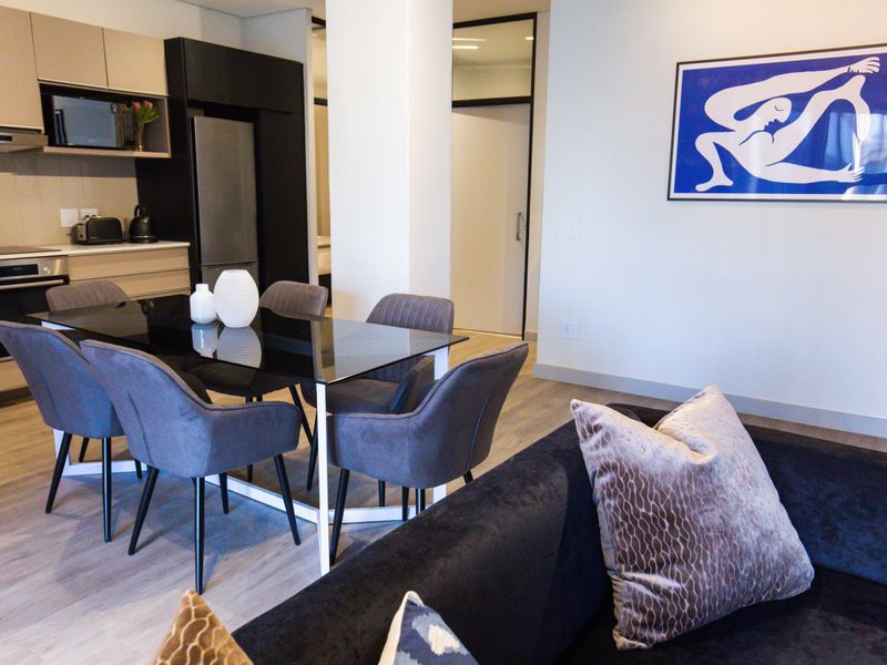 Modern open-plan living and dining area featuring a sleek kitchen with integrated appliances and contemporary laminate flooring.