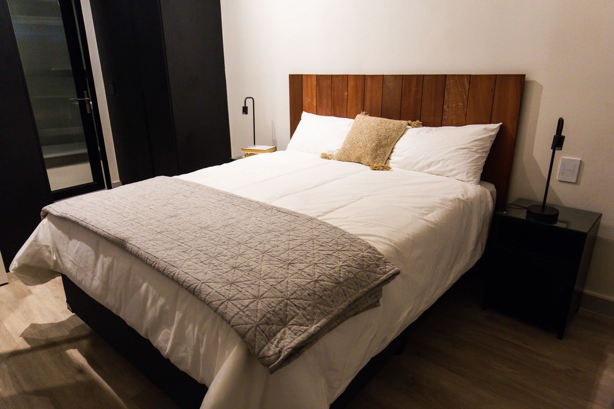A modern bedroom featuring light laminate flooring, a custom timber headboard, and a sleek built-in wardrobe.