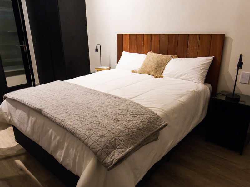 A modern bedroom featuring light laminate flooring, a custom timber headboard, and a sleek built-in wardrobe.