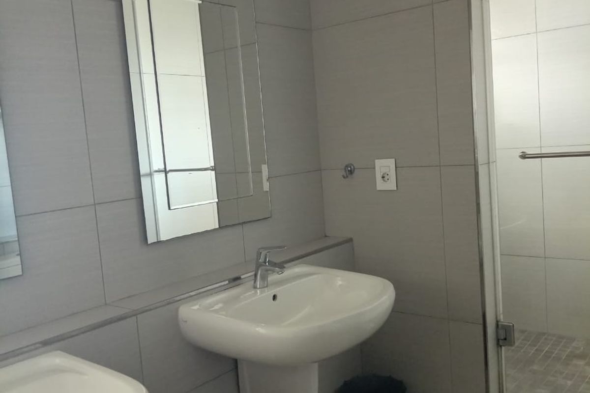 Modern bathroom featuring dual pedestal washbasins, a glass-enclosed shower, and neutral grey wall tiling.