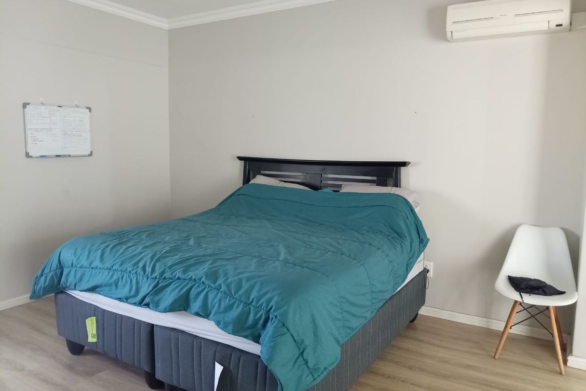 A well-maintained bedroom featuring light-toned laminate flooring, crown molding, and a wall-mounted split-system air conditioning unit.