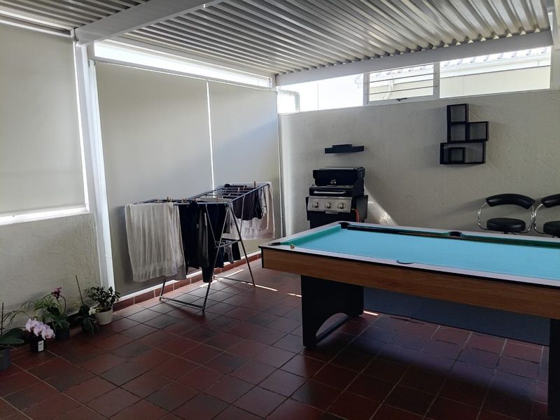 A covered patio area featuring tiled flooring, corrugated metal roofing, and adjustable roller blinds, suitable for outdoor entertainment.