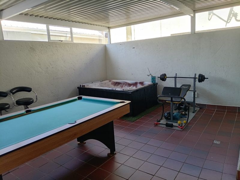 Covered patio area featuring a built-in jacuzzi, tiled flooring, and high-level windows, suitable for an entertainment or leisure space.