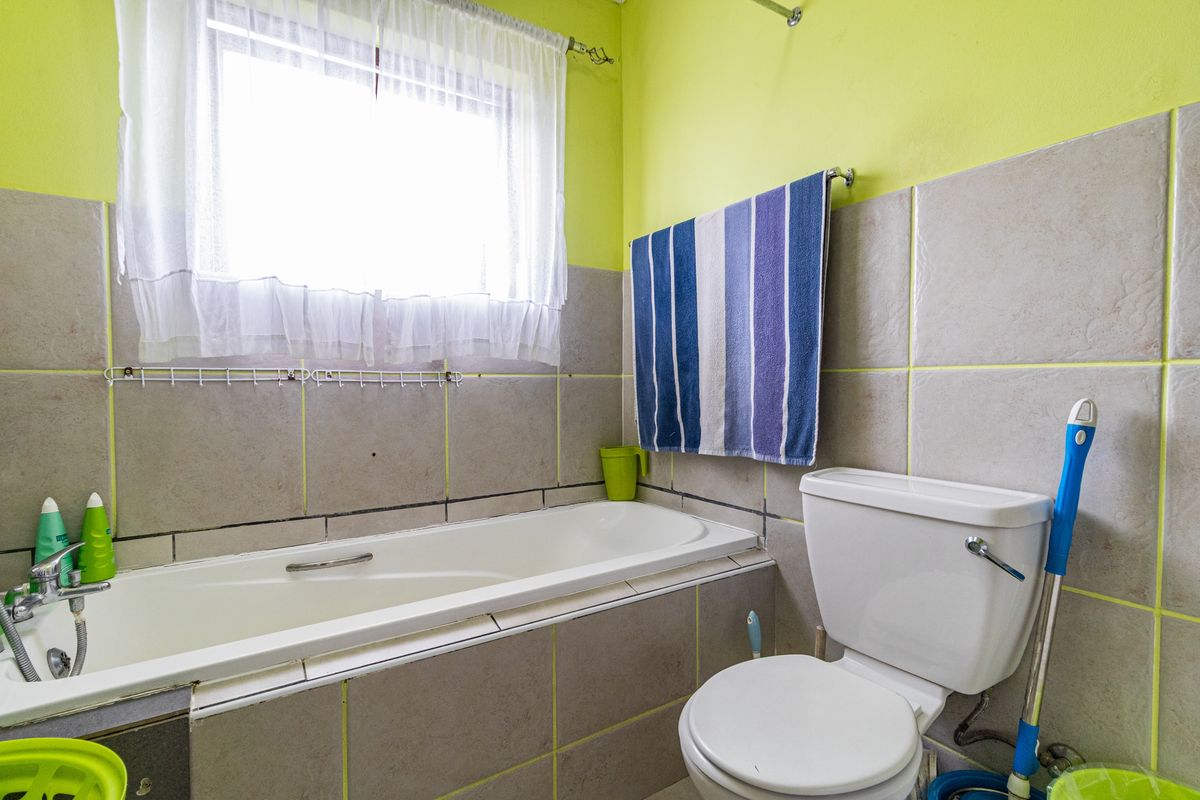 A functional bathroom featuring a bathtub, toilet, and neutral wall tiling with bright accent walls, offering a practical layout for daily use.