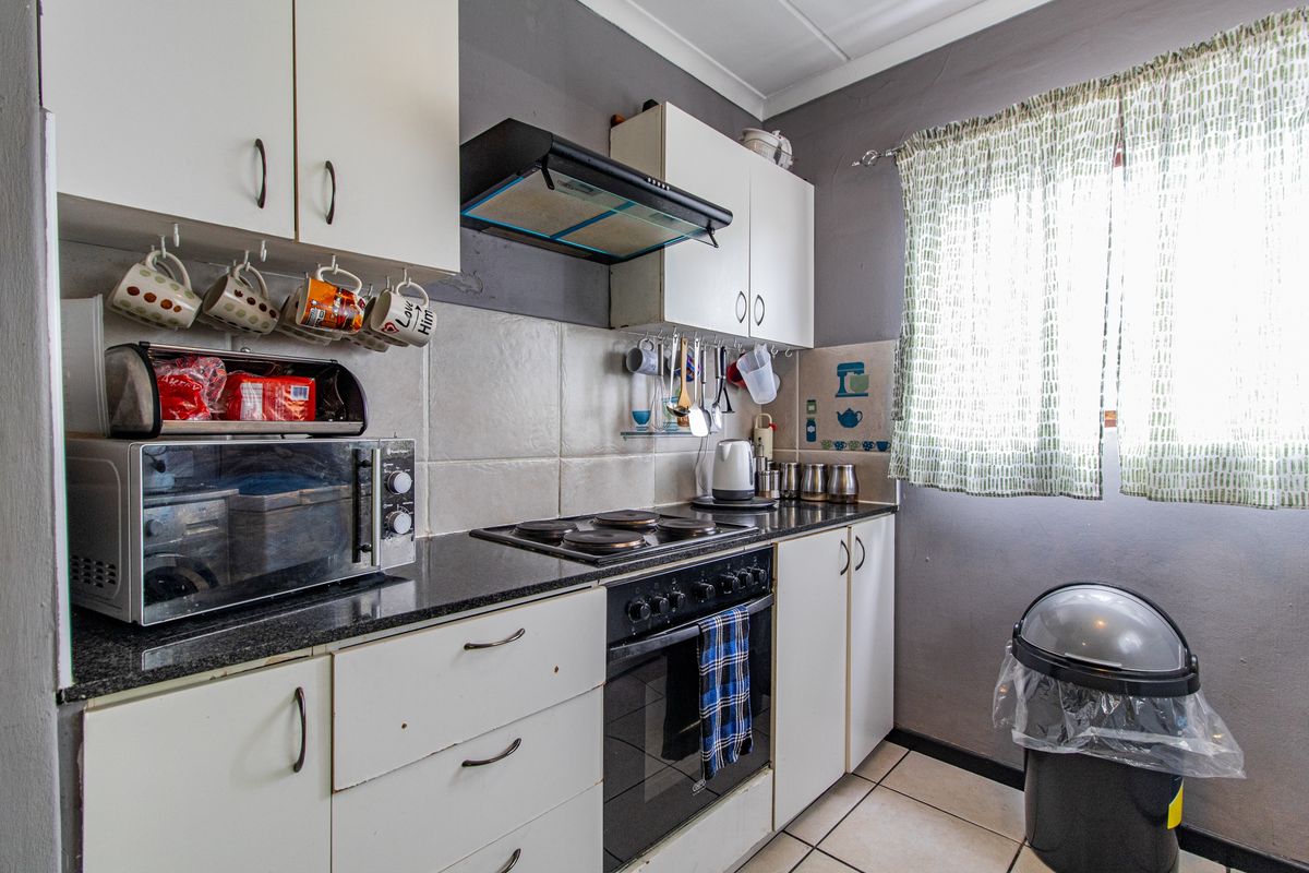 Compact kitchen featuring white built-in cabinetry, granite countertops, an electric hob, oven, and extractor fan with tiled backsplash and flooring.