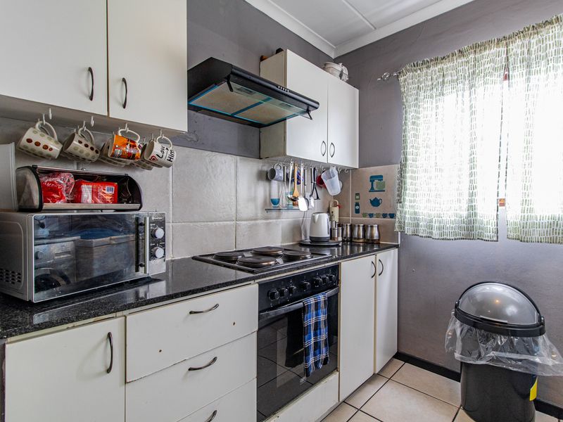 Compact kitchen featuring white built-in cabinetry, granite countertops, an electric hob, oven, and extractor fan with tiled backsplash and flooring.