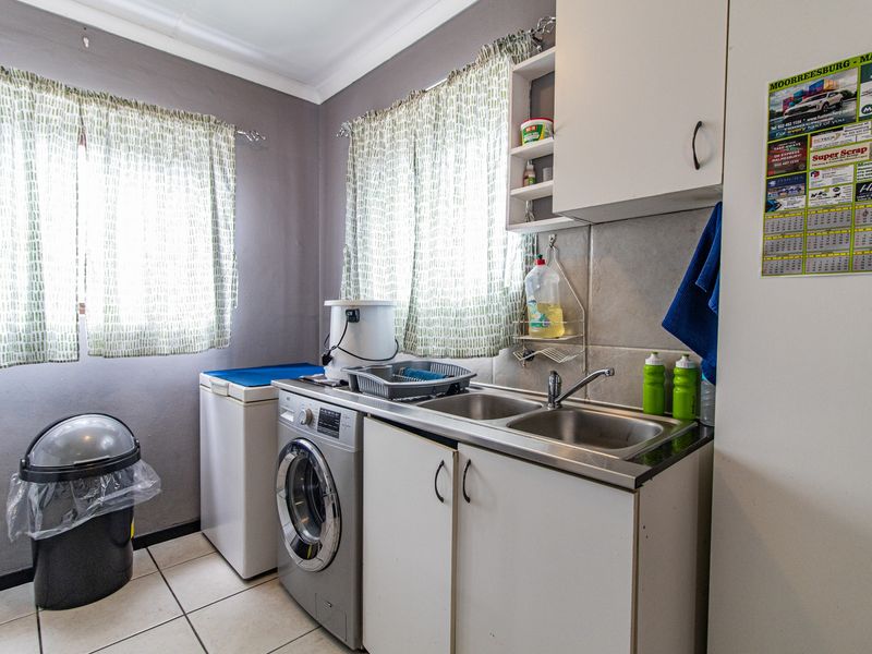 A functional laundry room featuring a stainless steel double sink, built-in cabinetry, and tiled flooring with dual windows for natural light.