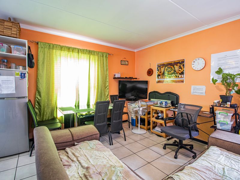 An open-plan living area featuring ceramic floor tiles and bright orange wall paint, offering a functional space for dining and relaxation.