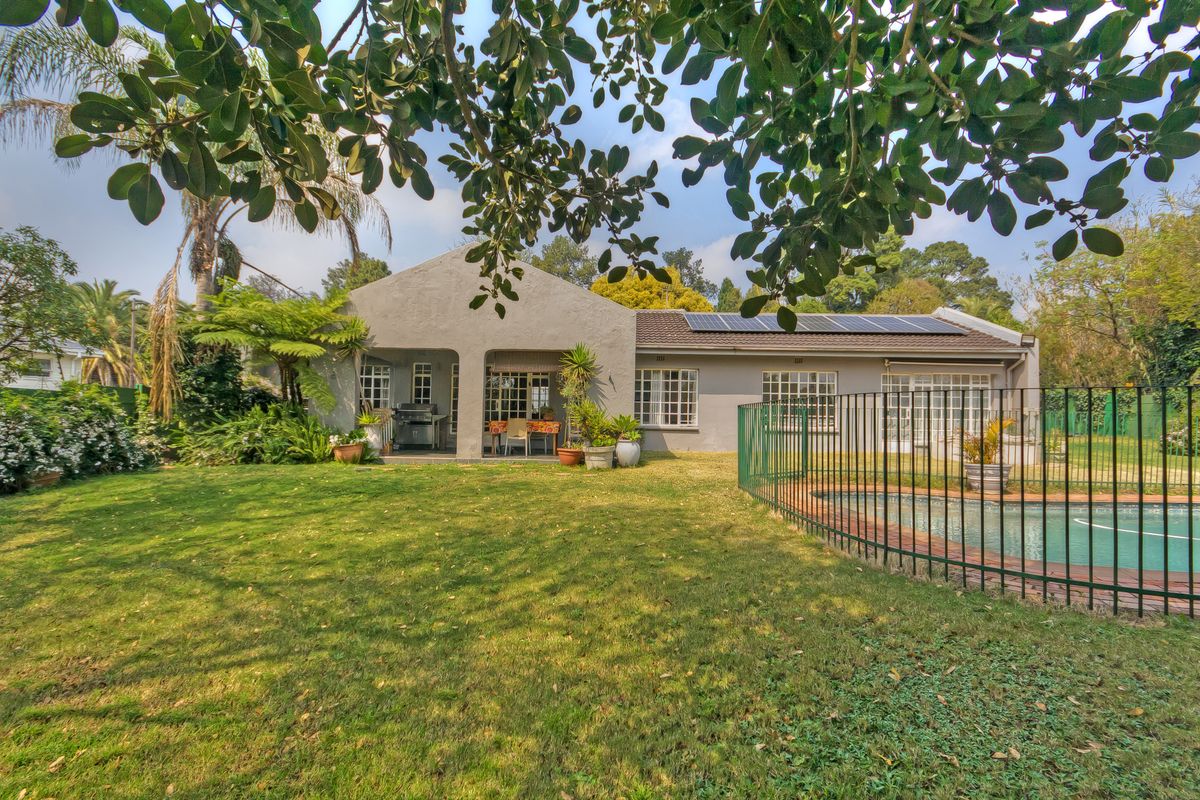 Rear view of the property featuring a well-maintained garden, swimming pool with safety fencing, covered patio area, and roof-mounted solar panels.