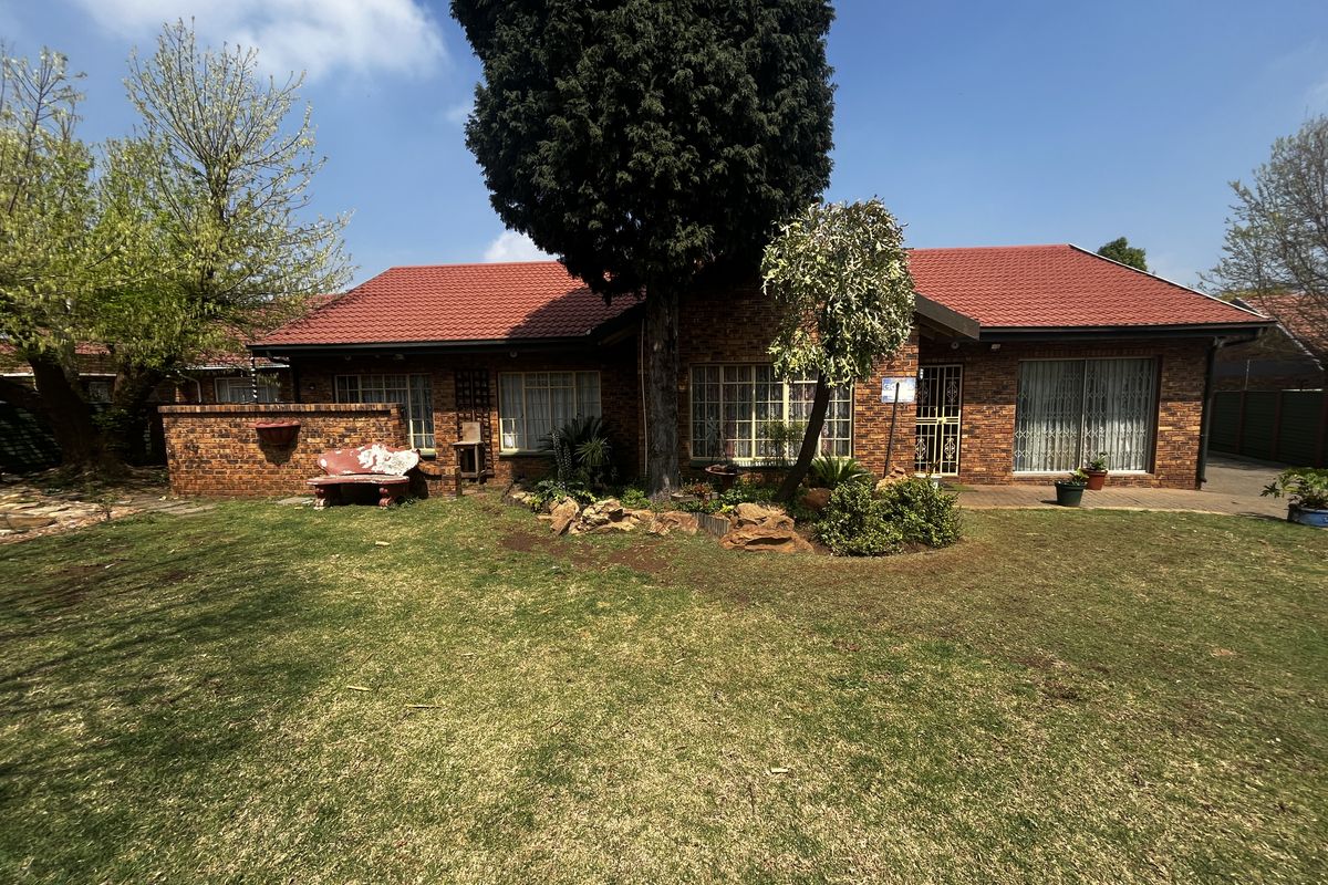A rear view of a single-story brick house featuring a tiled roof, paved patio area, and a well-maintained lawn.