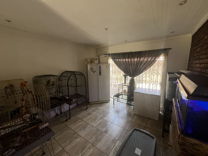 A living area featuring tiled flooring, an exposed brick feature wall, and a sliding glass door with security gate access to the exterior.