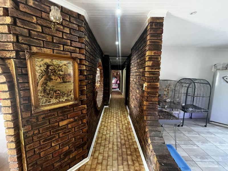 A long hallway featuring distinctive exposed brick walls, tiled flooring, and recessed ceiling lighting, connecting various areas of the home.