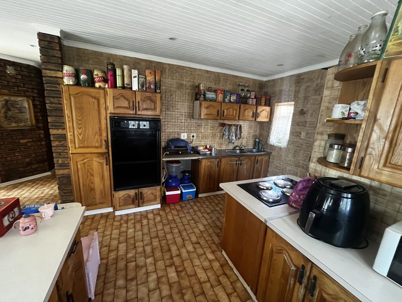 A functional kitchen featuring wooden cabinetry, built-in oven, electric hob, double sink, and a distinctive brick feature wall with tiled flooring.