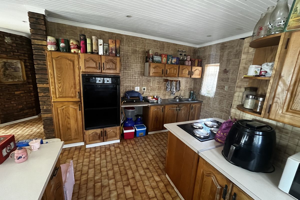 A functional kitchen featuring wooden cabinetry, built-in oven, electric hob, double sink, and a distinctive brick feature wall with tiled flooring.