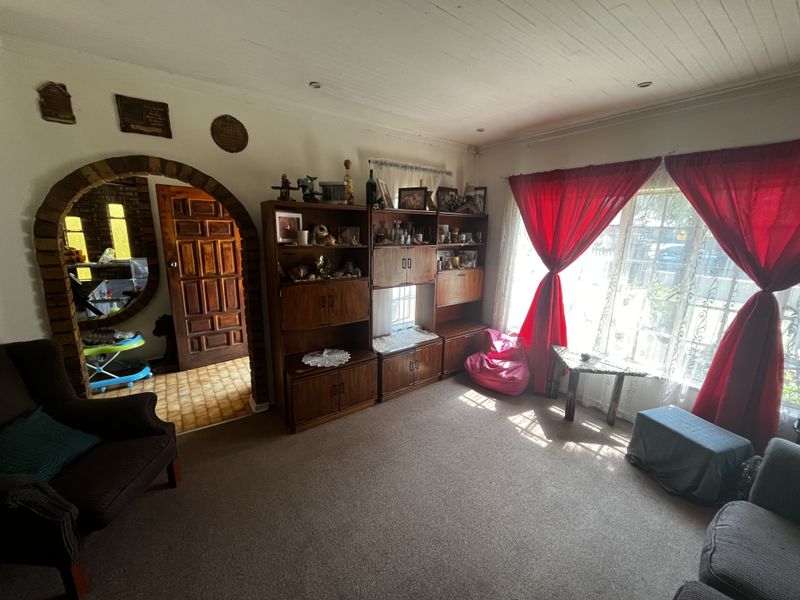 A living room featuring a distinctive brick archway, timber ceiling, and carpeted flooring, with natural light entering through a large window.