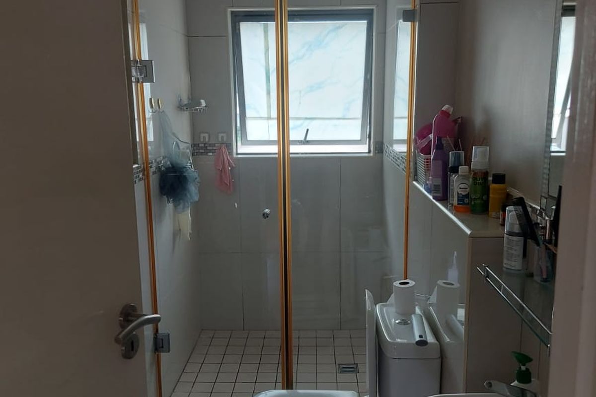 A compact bathroom featuring a tiled shower enclosure, pedestal basin, and toilet with neutral wall tiling.