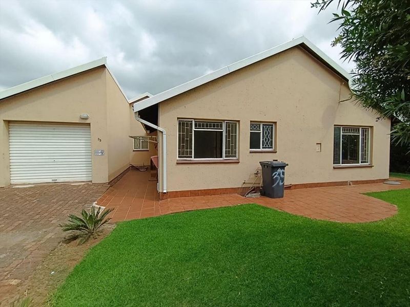 Front view of a townhouse featuring a single garage, paved driveway, tiled patio area, and a well-maintained lawn.
