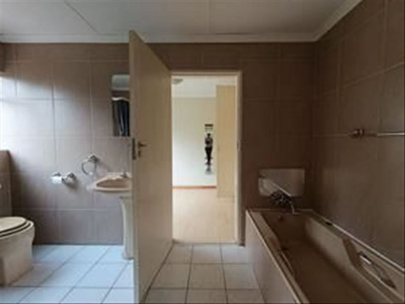 A dated bathroom featuring a pedestal basin, built-in bathtub, and toilet with full-height wall tiling.