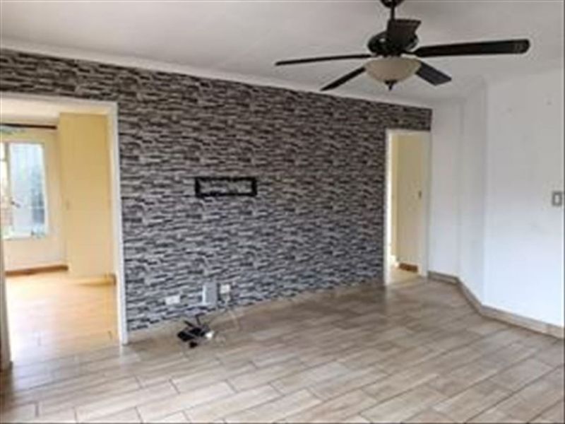 An empty living room featuring tiled flooring, a ceiling fan, and a prominent textured feature wall with dual access points to adjacent rooms.