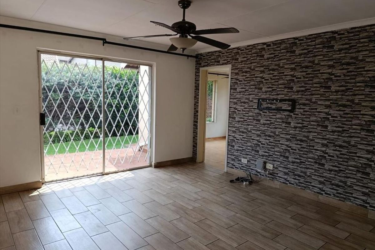 An empty living room featuring tiled floors, a stone-cladding feature wall, a ceiling fan, and a sliding glass door leading to the patio.