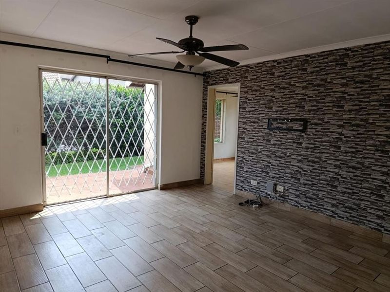 An empty living room featuring tiled floors, a stone-cladding feature wall, a ceiling fan, and a sliding glass door leading to the patio.