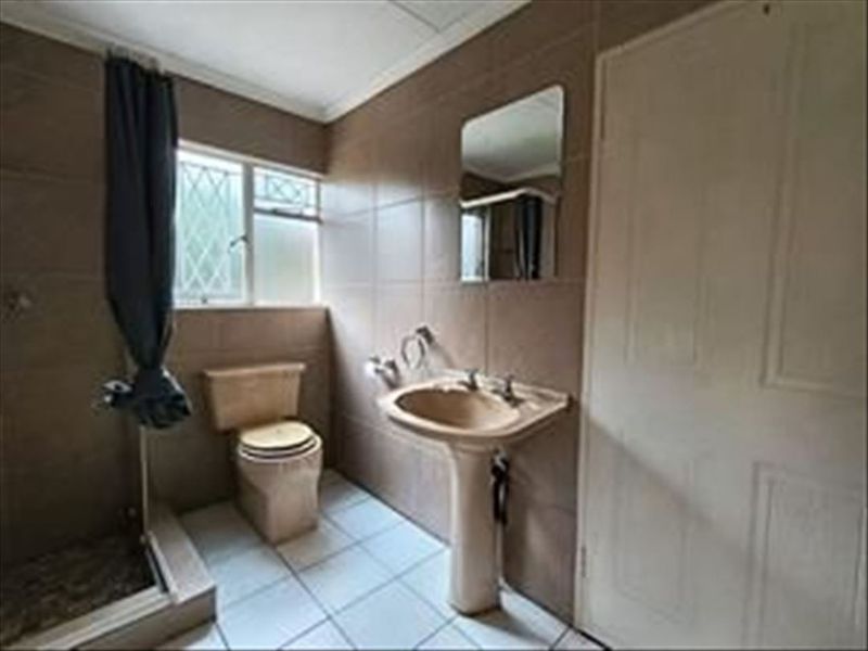 A dated bathroom featuring a pedestal basin, toilet, and shower enclosure with tiled walls and flooring, offering potential for modernization.