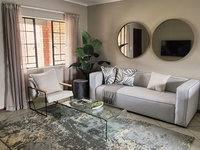 A well-maintained living room featuring neutral wall tones, tiled flooring, and a window with security bars, providing a comfortable and functional living space.