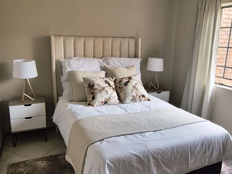 A well-maintained bedroom featuring neutral wall tones, tiled flooring, and a functional ceiling-mounted spotlight fixture.