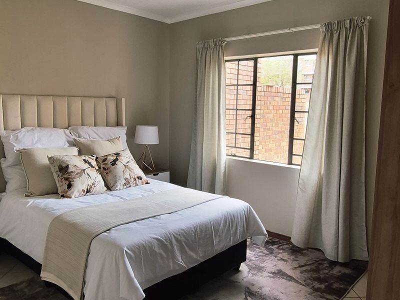 A well-maintained bedroom featuring neutral wall tones, tiled flooring, and a window with security bars, providing a comfortable and functional living space.