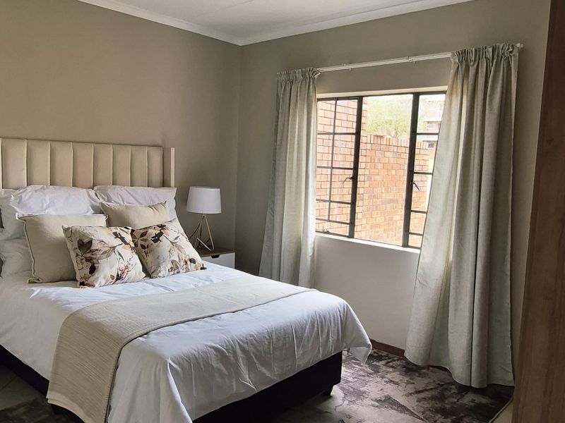 A well-maintained bedroom featuring tiled flooring, a window with security bars, and a modern ceiling-mounted spotlight fixture.