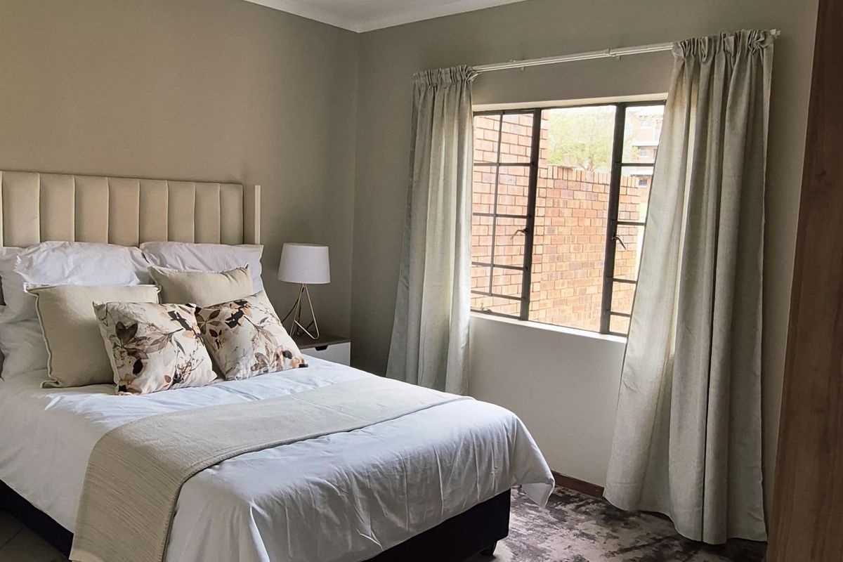 A well-maintained bedroom featuring tiled flooring, a window with security bars, and a modern ceiling-mounted spotlight fixture.