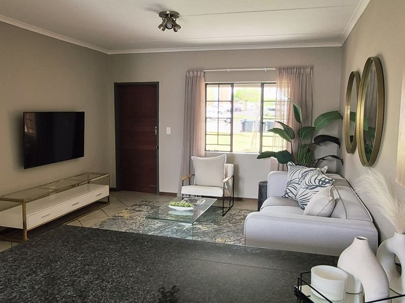 An open-plan living area featuring a modern kitchen with granite countertops and light wood cabinetry, seamlessly flowing into a comfortable lounge space.
