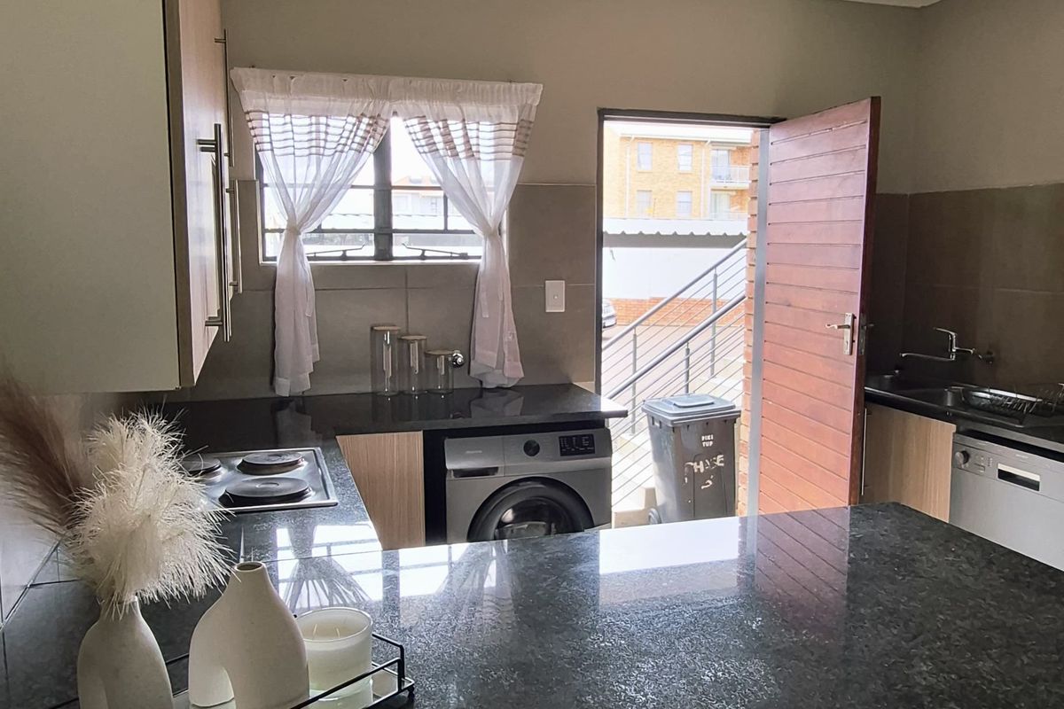 A functional kitchen featuring granite countertops, built-in cabinetry, and tiled flooring, with direct access to an outdoor area.