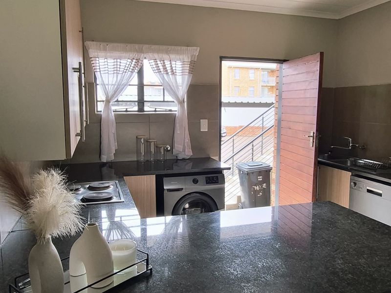 A functional kitchen featuring granite countertops, built-in cabinetry, and tiled flooring, with direct access to an outdoor area.