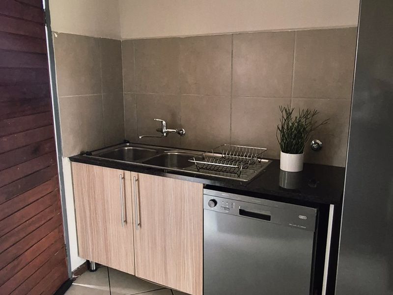 A functional scullery area featuring a double sink, tiled backsplash, laminate cabinetry, and space for a dishwasher with tiled flooring.