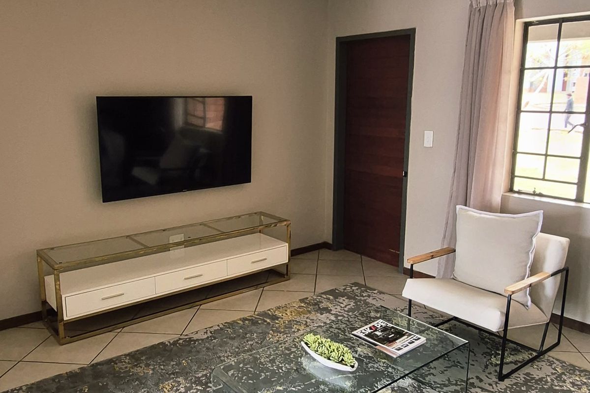 A well-maintained living room featuring neutral wall tones, tiled flooring, and a ceiling-mounted spotlight fixture, providing a comfortable and functional living space.