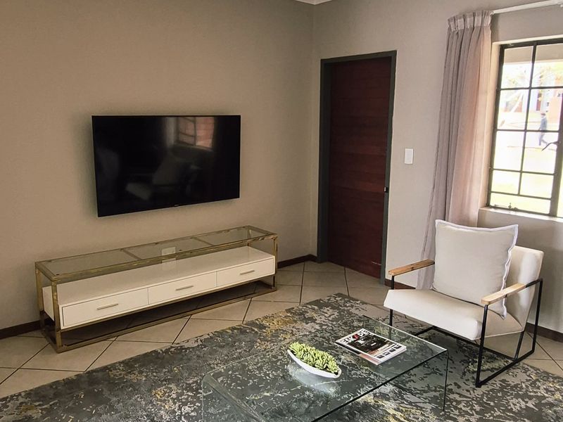 A well-maintained living room featuring neutral wall tones, tiled flooring, and a ceiling-mounted spotlight fixture, providing a comfortable and functional living space.