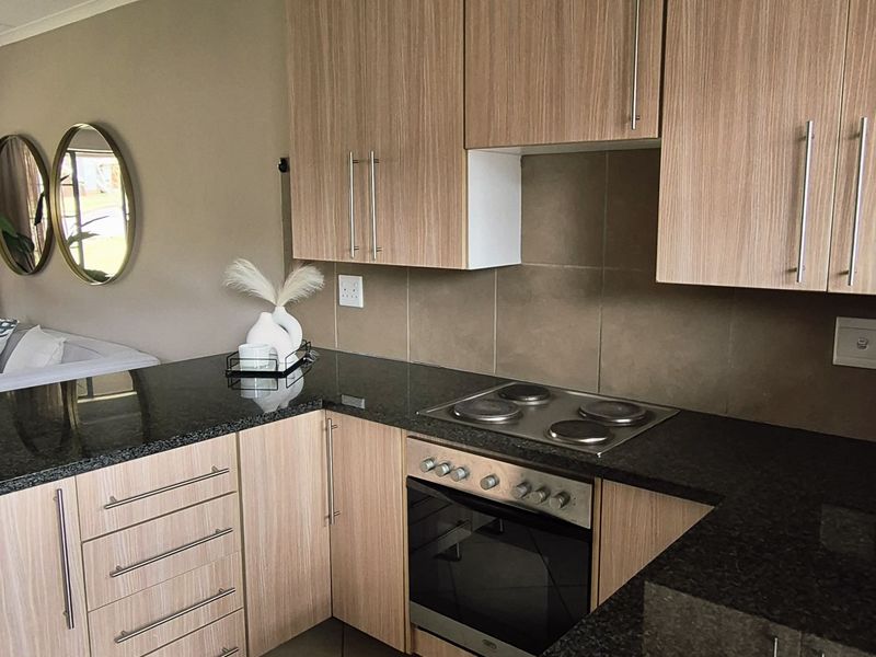A functional kitchen featuring light wood-grain cabinetry, dark granite countertops, a built-in electric oven, and a hob with a tiled backsplash.