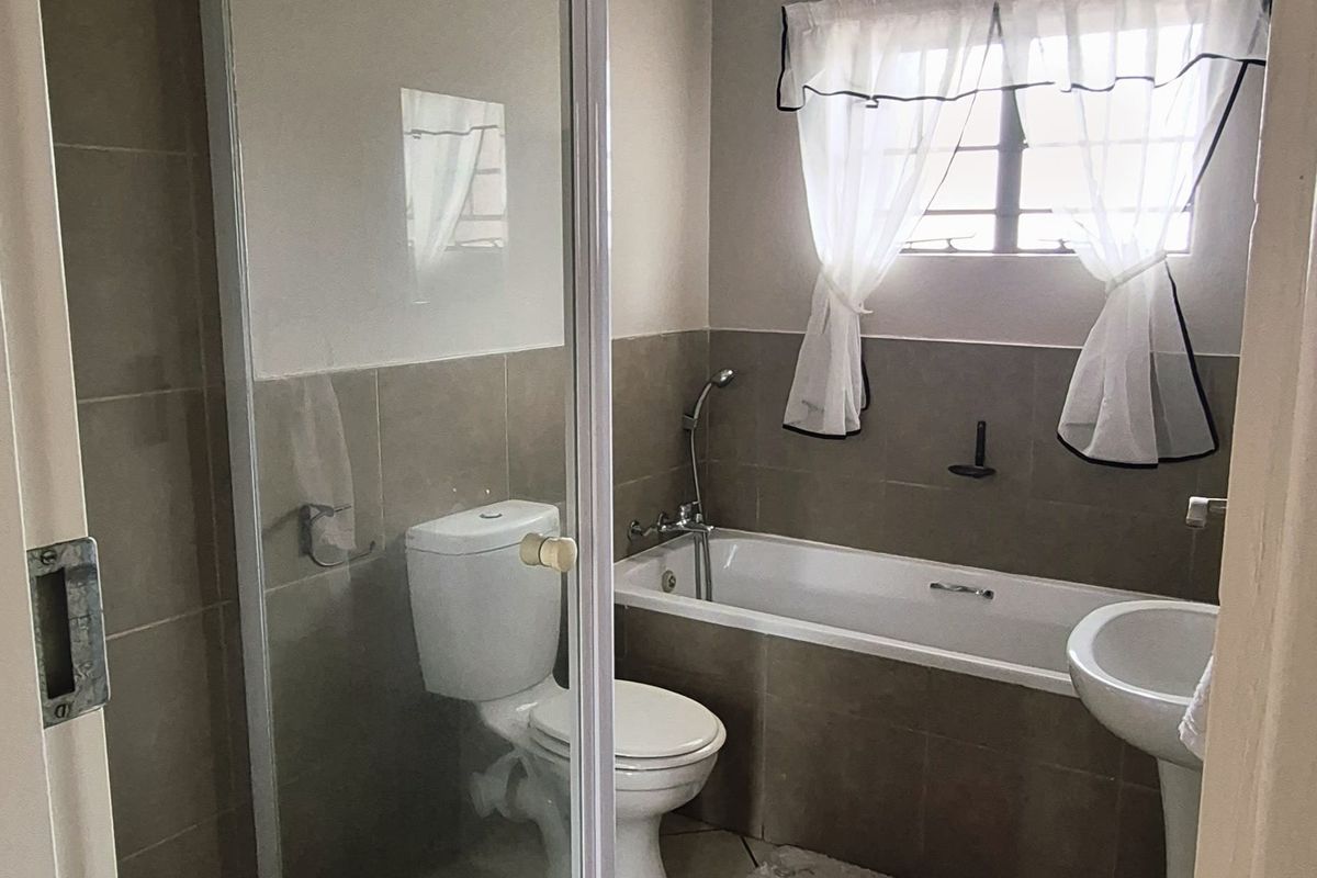 A functional bathroom featuring a glass-enclosed shower, a built-in bathtub, a pedestal basin, and neutral wall and floor tiling.