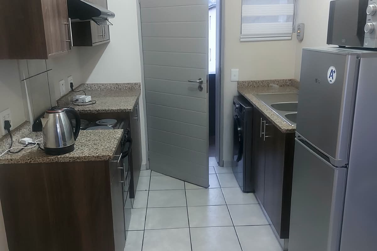 A functional galley-style kitchen featuring dark wood cabinetry, granite countertops, tiled flooring, and integrated appliance space.