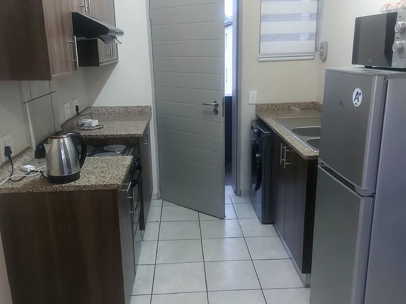 A functional galley-style kitchen featuring dark wood cabinetry, granite countertops, tiled flooring, and integrated appliance space.