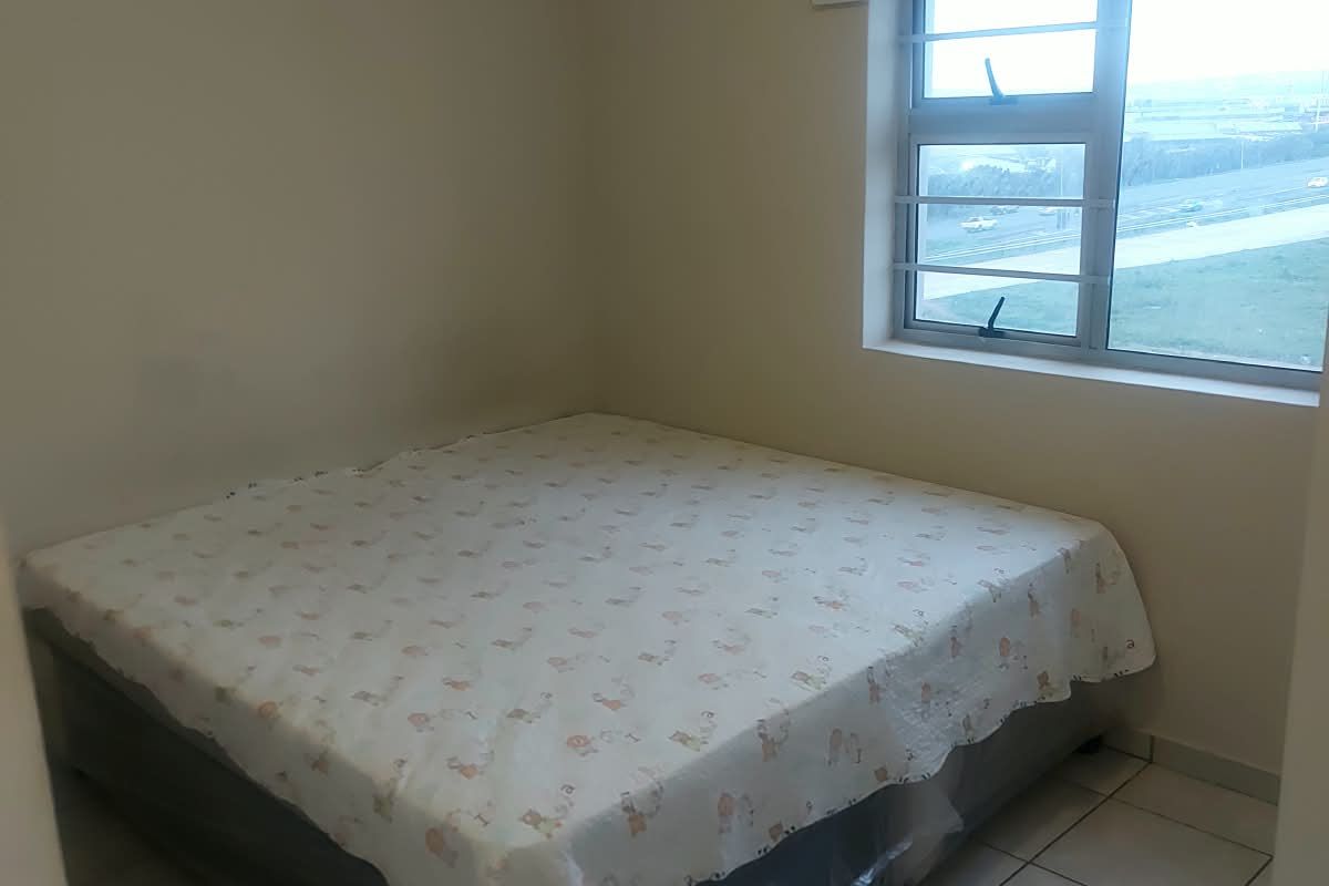 A simple bedroom featuring tiled flooring, a window with security bars, and a roller blind.