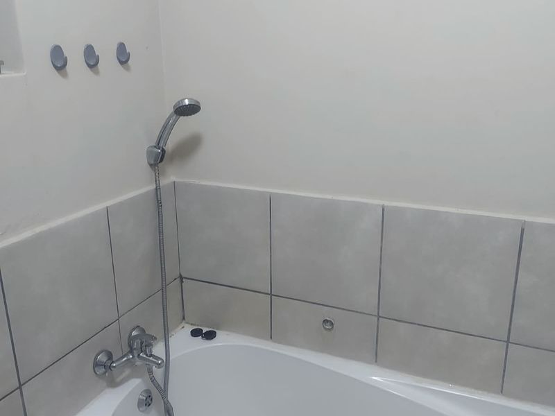 A functional bathroom featuring a standard bathtub with a handheld shower attachment and neutral wall tiling.