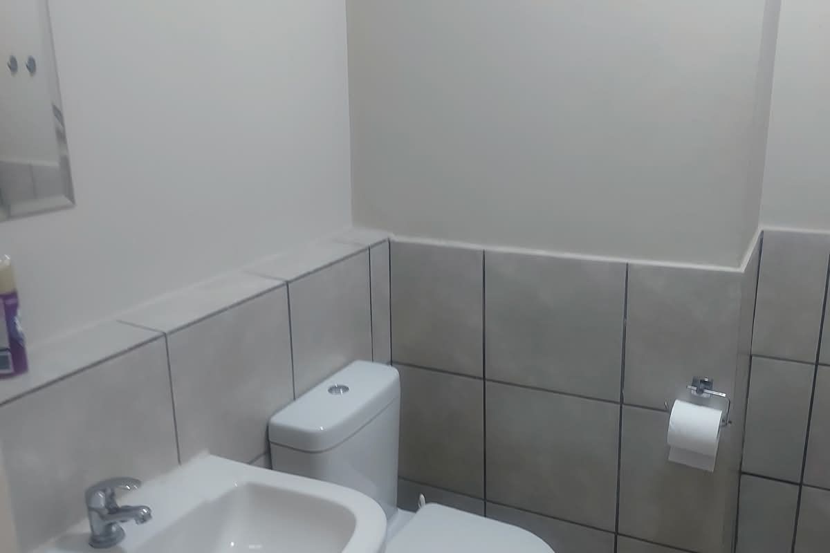 A functional bathroom featuring a pedestal basin, toilet, and neutral wall and floor tiling.