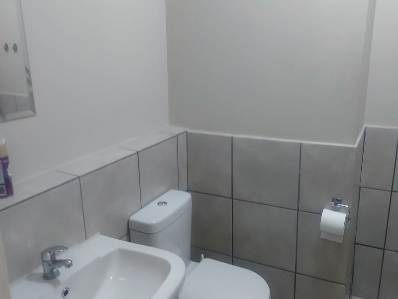 A functional bathroom featuring a pedestal basin, toilet, and neutral wall and floor tiling.
