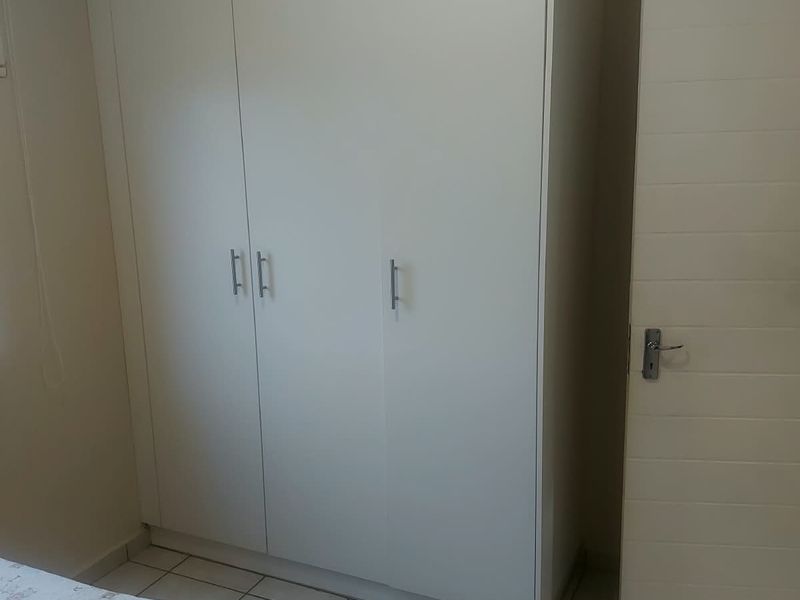 A bedroom featuring a large white built-in wardrobe, tiled flooring, and a standard internal door.