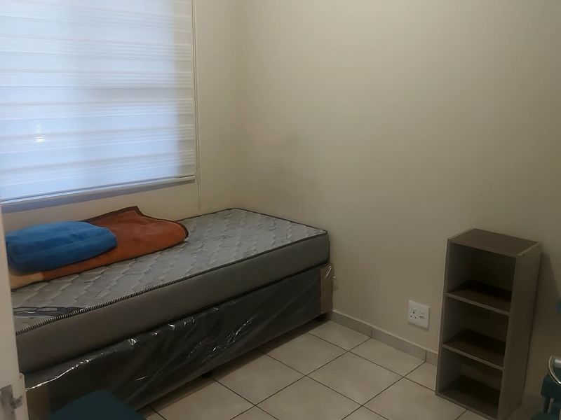A compact bedroom featuring neutral wall paint, tiled flooring, and a window fitted with a roller blind.