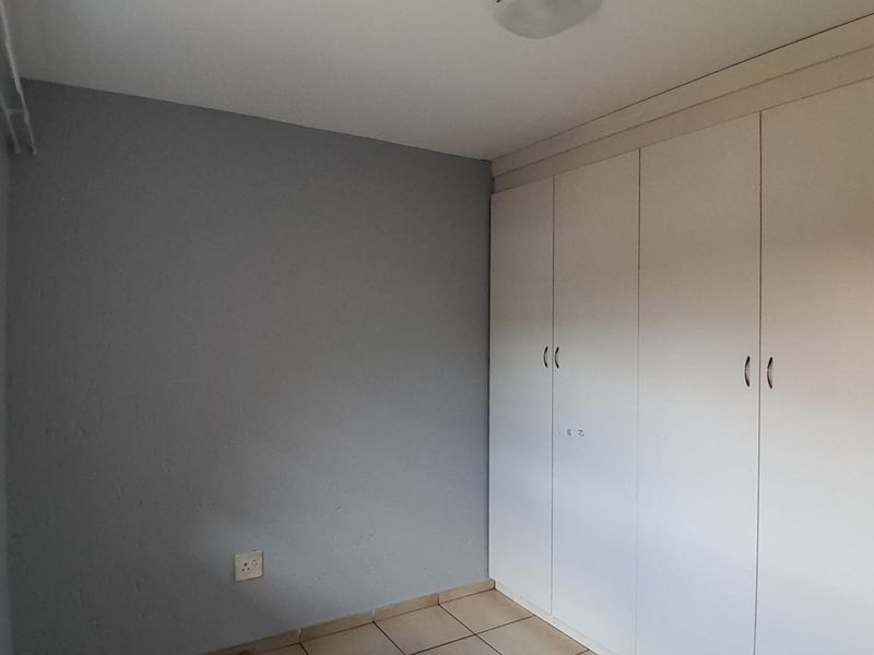 A clean, empty bedroom featuring neutral grey walls, tiled flooring, and ample built-in cupboard storage space.